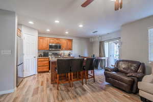 Kitchen with a breakfast bar, a kitchen island with sink, light hardwood / wood-style flooring, ceiling fan, and stainless steel appliances