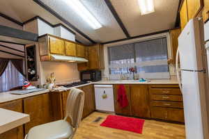 Kitchen with sink, a textured ceiling, lofted ceiling, white appliances, and light wood-type flooring