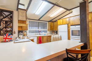 Kitchen with sink, kitchen peninsula, white appliances, lofted ceiling, and a breakfast bar area