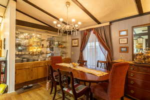 Dining room featuring vaulted ceiling, light hardwood / wood-style floors, a textured ceiling, and an inviting chandelier