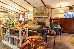 Living area featuring wood walls, lofted ceiling with beams, carpet flooring, a fireplace, and a textured ceiling