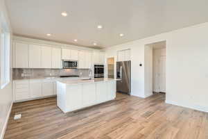 Kitchen with white cabinets, LVP, and appliances with stainless steel finishes