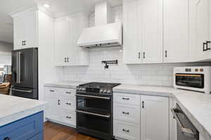 Kitchen with white cabinets, decorative backsplash, dark hardwood / wood-style flooring, custom range hood, and stainless steel appliances