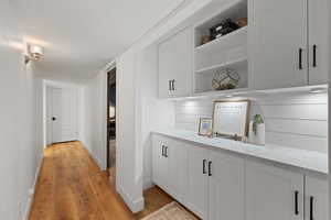 Bar featuring light stone counters, white cabinetry, a textured ceiling, and light hardwood / wood-style flooring