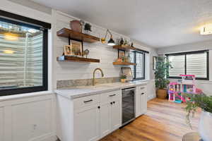 Kitchen featuring sink, beverage cooler, a textured ceiling, white cabinets, and light wood-type flooring