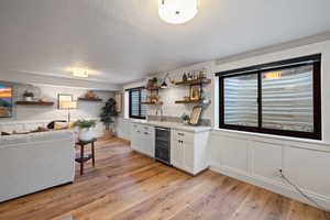 Kitchen with sink, beverage cooler, a textured ceiling, white cabinets, and light wood-type flooring