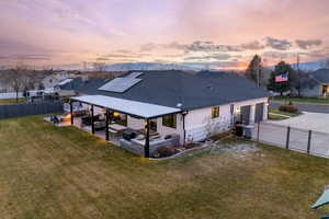 Back house at dusk with solar panels, central air condition unit, an outdoor hangout area, a yard, and a patio area