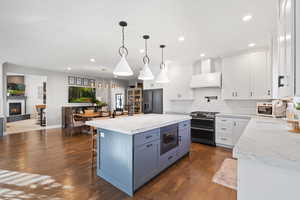 Kitchen with dark hardwood / wood-style flooring, stainless steel appliances, decorative light fixtures, white cabinetry, and a large island