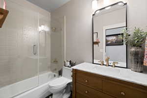 Full bathroom with vanity, bath / shower combo with glass door, and toilet