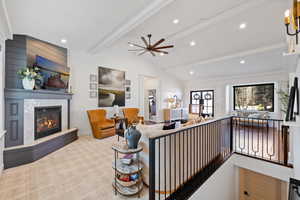 Living room with lofted ceiling with beams, ceiling fan, ornamental molding, and a tile fireplace