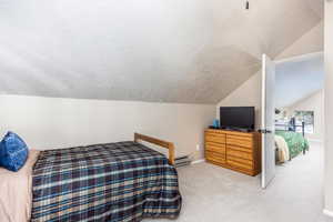 Carpeted bedroom featuring a textured ceiling, vaulted ceiling, and baseboard heating