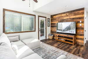 Living room with ceiling fan, wood walls, and dark wood-type flooring