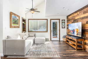 Living room featuring vaulted ceiling, baseboard heating, dark wood-type flooring, and ceiling fan