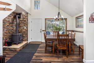 Dining room with a notable chandelier, dark hardwood / wood-style flooring, a wood stove, and high vaulted ceiling