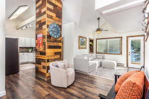 Living room with dark wood-type flooring, high vaulted ceiling, ceiling fan, baseboard heating, and beam ceiling