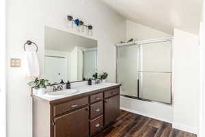 Bathroom with hardwood / wood-style flooring, a textured ceiling, bath / shower combo with glass door, and vaulted ceiling