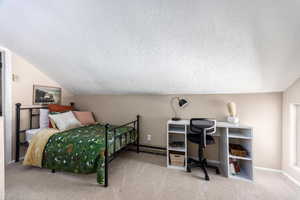 Carpeted bedroom featuring a textured ceiling and vaulted ceiling