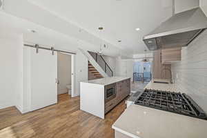 Kitchen with island exhaust hood, appliances with stainless steel finishes, sink, pendant lighting, and hardwood / wood-style floors