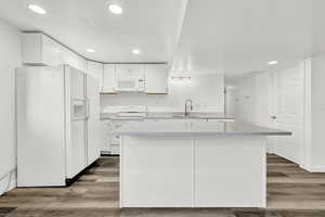 Kitchen with white cabinets, wood-type flooring, white appliances, and sink