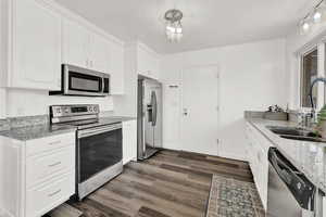 Kitchen featuring white cabinets, sink, light stone counters, dark hardwood / wood-style flooring, and stainless steel appliances