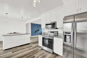 Kitchen featuring appliances with stainless steel finishes, light wood-type flooring, stone counters, white cabinets, and hanging light fixtures