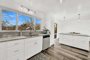 Kitchen with pendant lighting, sink, stainless steel dishwasher, dark hardwood / wood-style floors, and white cabinetry