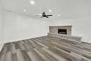 Unfurnished living room featuring a stone fireplace, ceiling fan, and wood-type flooring