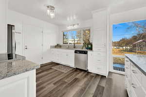 Kitchen with dark hardwood / wood-style flooring, light stone counters, stainless steel appliances, sink, and white cabinets