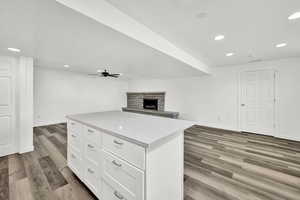 Kitchen featuring white cabinetry, a center island, ceiling fan, dark wood-type flooring, and light stone counters