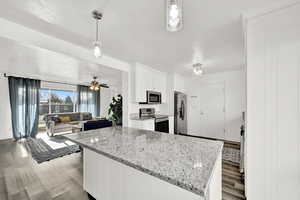 Kitchen with light stone countertops, dark wood-type flooring, pendant lighting, white cabinets, and appliances with stainless steel finishes