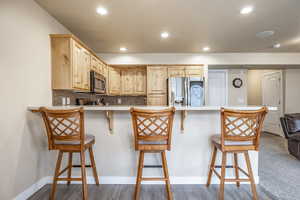 Kitchen featuring kitchen peninsula, a kitchen breakfast bar, stainless steel appliances, light brown cabinets, and wood-type flooring