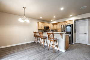 Kitchen with an inviting chandelier, light hardwood / wood-style floors, pendant lighting, a breakfast bar area, and appliances with stainless steel finishes