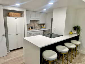 Kitchen with a kitchen breakfast bar, backsplash, sink, and light hardwood / wood-style flooring