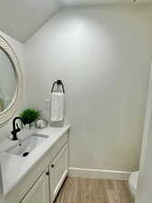 Bathroom with hardwood / wood-style floors, vanity, toilet, and vaulted ceiling