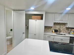 Kitchen with light hardwood / wood-style floors, stovetop, white cabinetry, and sink