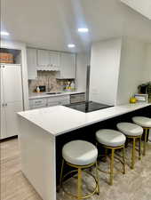 Kitchen with backsplash, light hardwood / wood-style flooring, a breakfast bar area, and sink