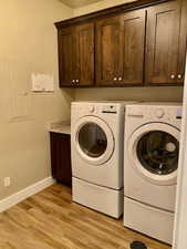 Laundry area with cabinets, washing machine and dryer, electric panel, and light hardwood / wood-style flooring