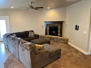 Living room featuring hardwood / wood-style flooring, ceiling fan, a stone fireplace, and a textured ceiling