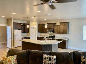 Kitchen featuring light stone counters, decorative light fixtures, dark brown cabinets, a center island with sink, and appliances with stainless steel finishes