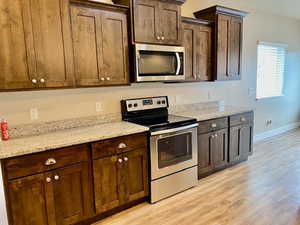 Kitchen featuring dark brown cabinetry, light stone countertops, light hardwood / wood-style flooring, and appliances with stainless steel finishes