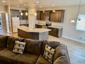 Kitchen with dark brown cabinets, stainless steel appliances, a center island with sink, light hardwood / wood-style floors, and hanging light fixtures