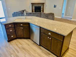 Kitchen with light stone countertops, stainless steel dishwasher, sink, light hardwood / wood-style floors, and a stone fireplace