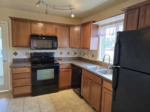 Kitchen with black appliances, backsplash, light tile patterned floors, and sink