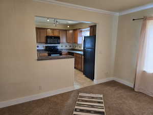 Kitchen with black appliances, crown molding, light colored carpet, and backsplash