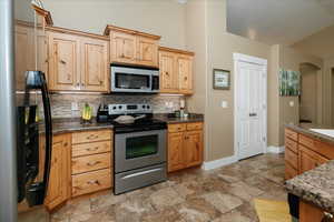 Kitchen featuring appliances, backsplash, dark stone counters, and light brown cabinetry