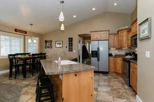 Kitchen with a kitchen breakfast bar, silver appliances, vaulted ceiling, a spacious island, and sink