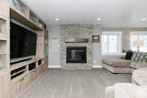 Living room with carpet flooring, a stone fireplace, and a textured ceiling