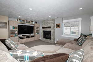 Living room featuring a stone fireplace, carpet floors, and a textured ceiling