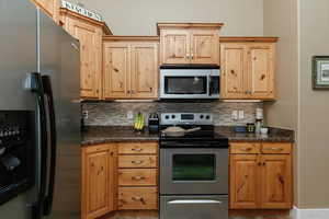 Kitchen with dark countertops, decorative backsplash, light brown cabinetry, and stainless steel appliances