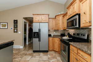 Kitchen featuring decorative backsplash, dark countertops, and vaulted ceiling